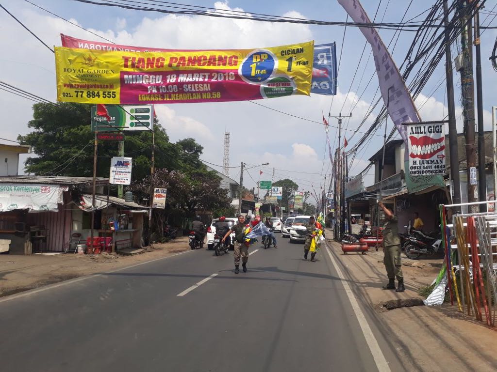 Satpol PP Kota Depok menurunkan spanduk liar di Jalan Raya Sawangan. 